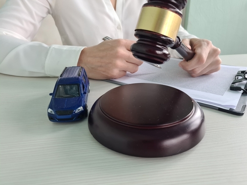A car accident lawyer near a car and gavel helping a victim of a car crash with their case.