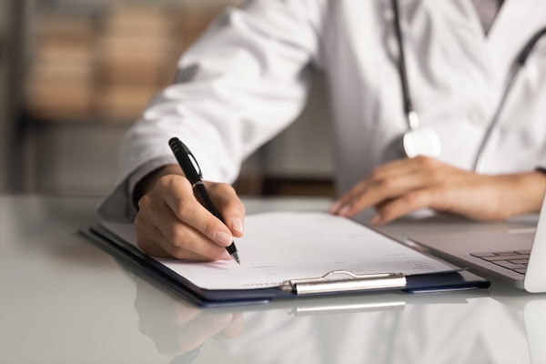 A doctor with a clipboard writes medical records for a car accident claim.